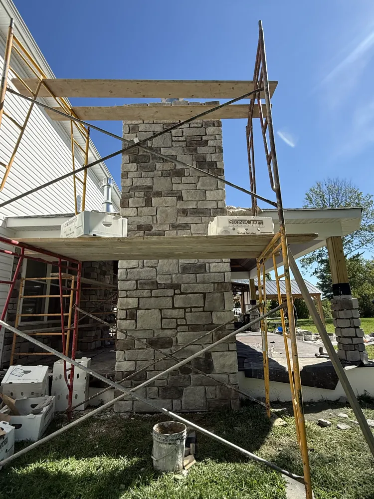 Stone veneer chimney under construction with scaffolding in place