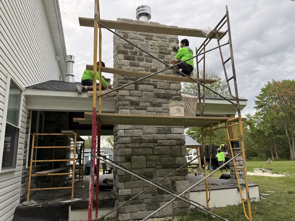 Two crew members installing stone veneer on a two-story chimney